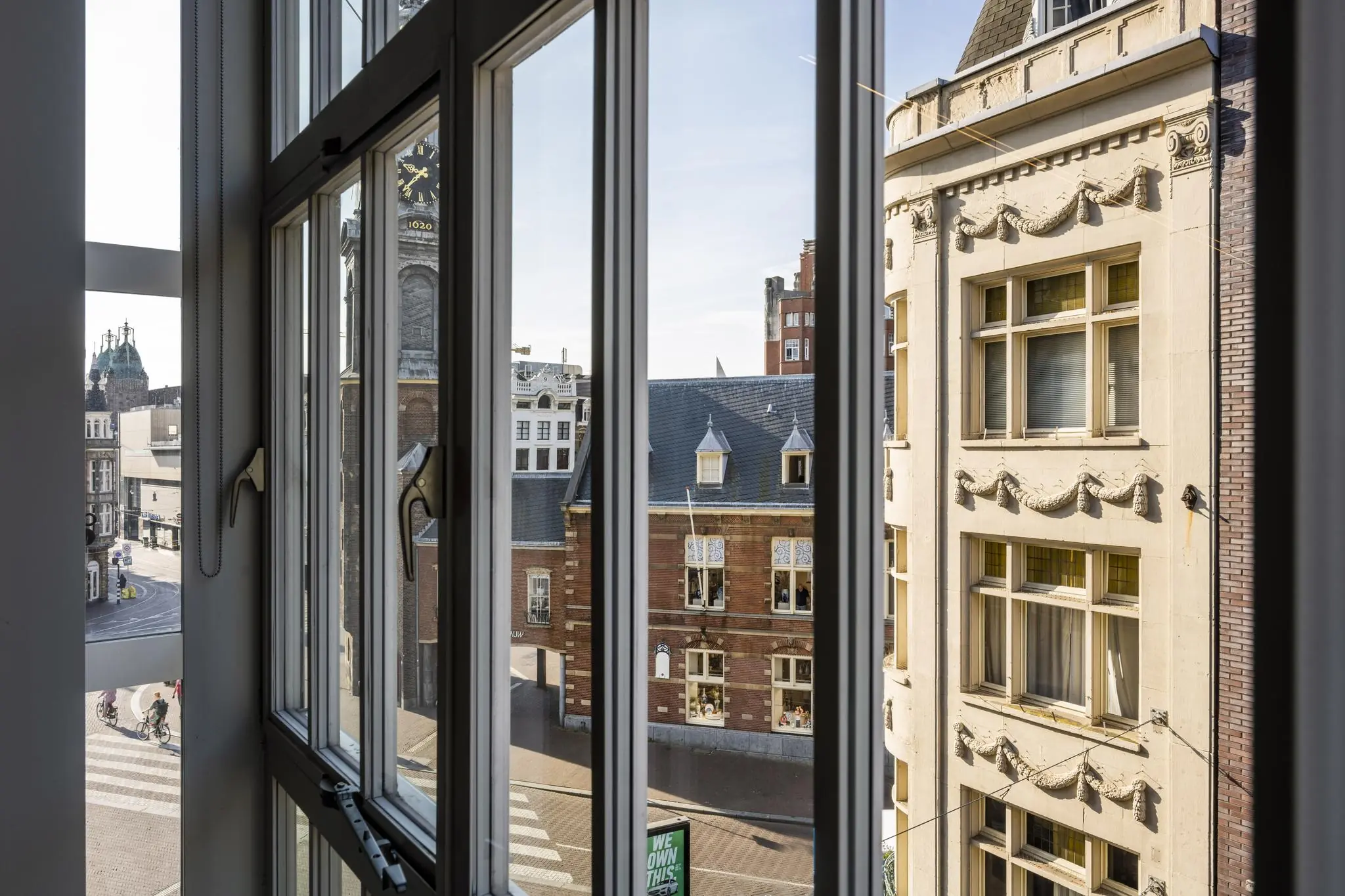 Uitzicht vanuit een raam op de Sint Jorissteeg met historische gebouwen en een torenklok in het centrum van Amsterdam.